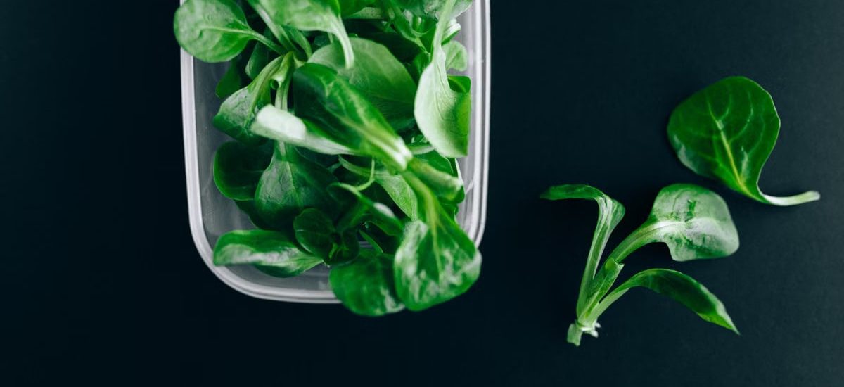 Close-up of fresh green salad leaves in a plastic container on a black background.