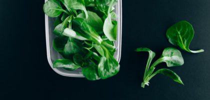 Close-up of fresh green salad leaves in a plastic container on a black background.