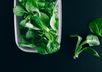 Close-up of fresh green salad leaves in a plastic container on a black background.